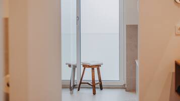 Un interior moderno con un taburete de madera y un banco blanco cerca de un vidrio que da a un balcón.