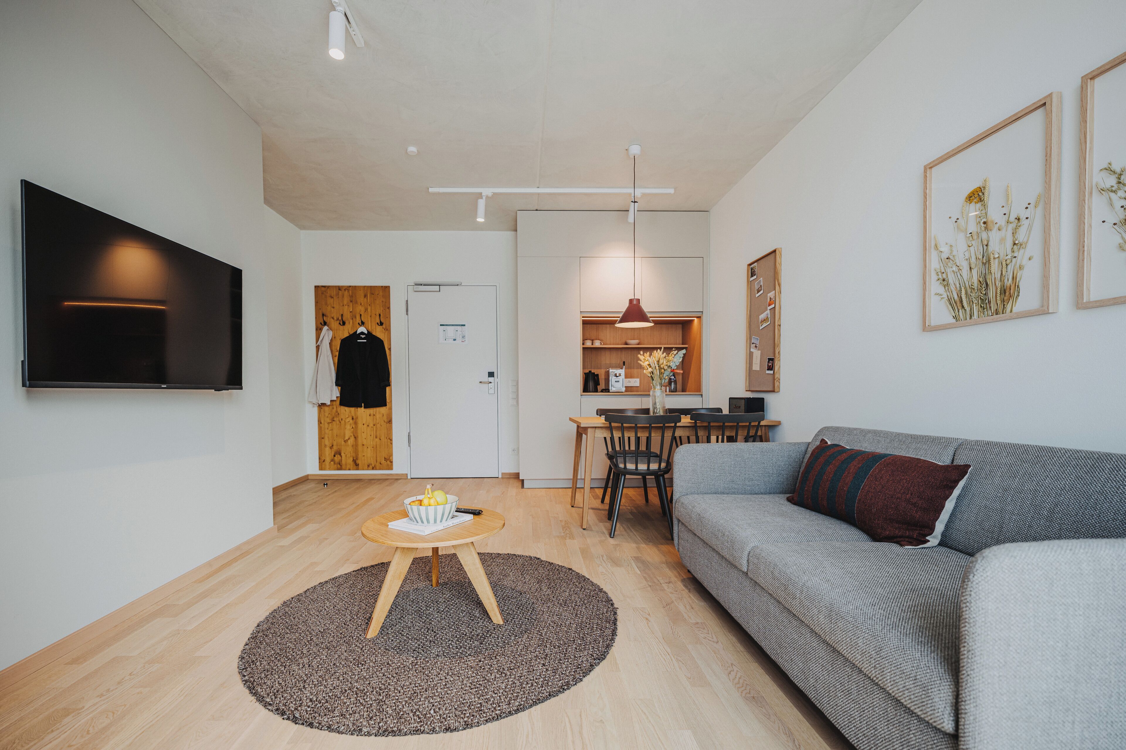 Una sala de estar moderna con un sofá gris, una mesa redonda de madera y un televisor de pantalla plana montado en la pared.