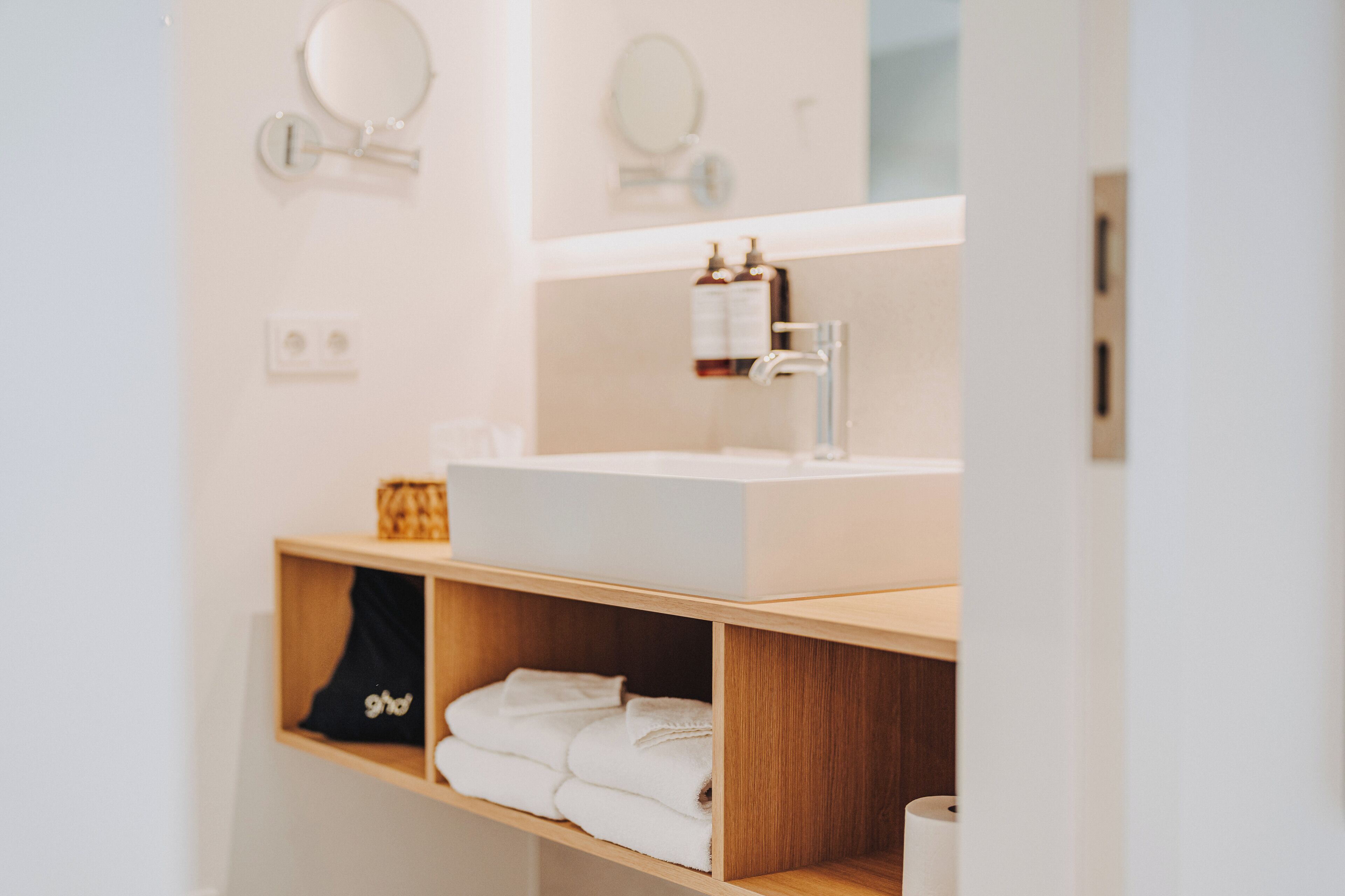 A modern bathroom with a white sink, two mirrors, and a shelf with folded towels.