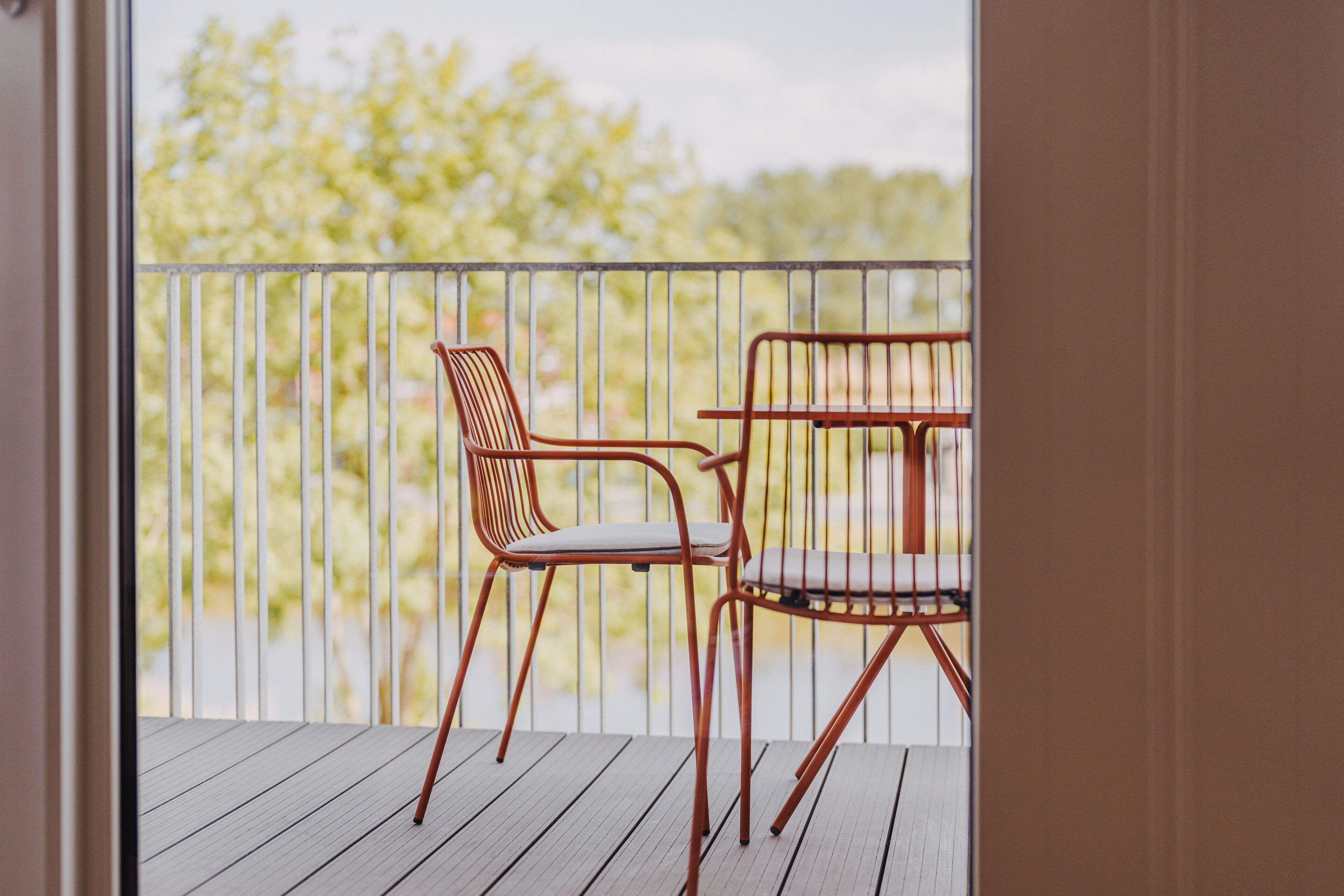 A balcony with a wooden floor, a metal railing, and two metal chairs with cushions.