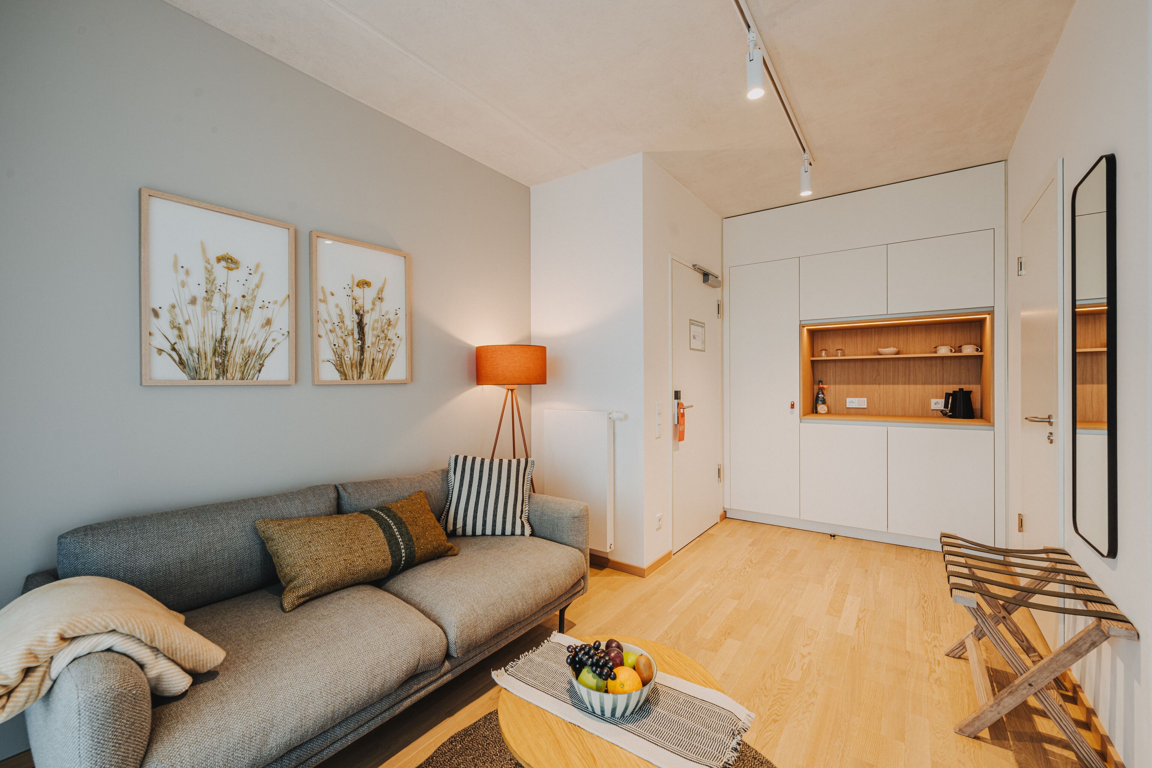 A modern living room with a grey sofa, a coffee table with fruit, and framed artwork on the wall.