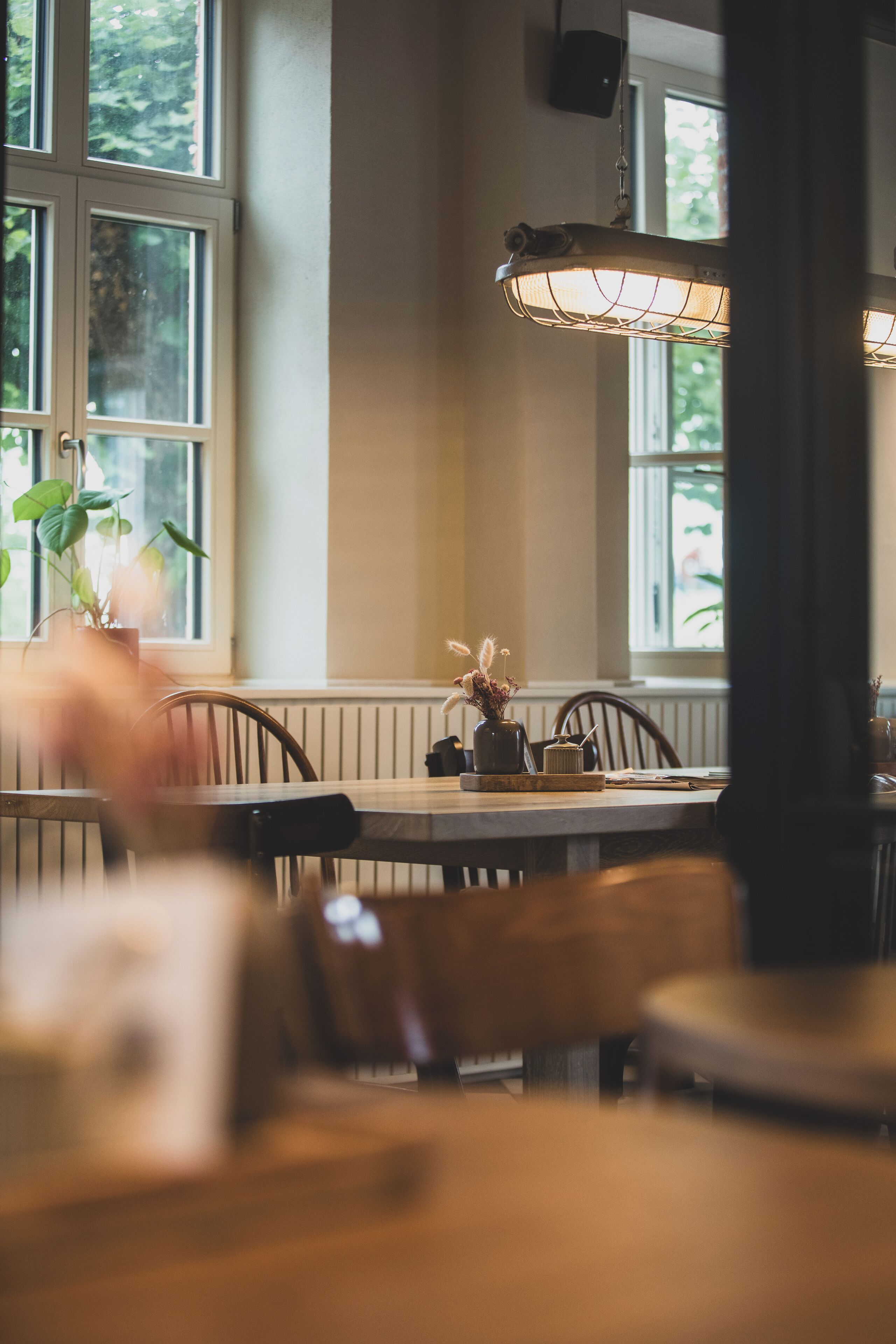 A dining area with a table, chairs, a hanging light fixture, and a window with a view of greenery.