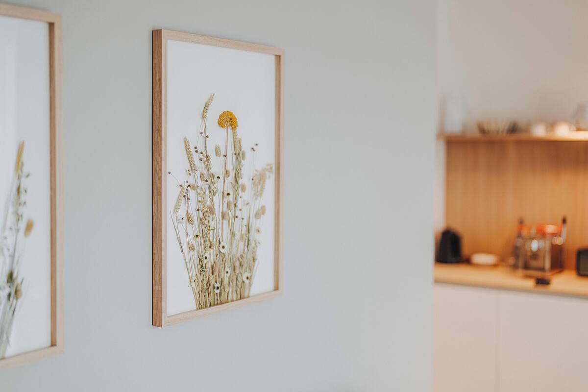 A framed botanical print on a wall, a kitchen area with wooden cabinets and a countertop, and a blurred background suggesting a residential setting.