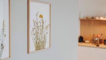 A framed botanical print on a wall, a kitchen area with wooden cabinets and a countertop, and a blurred background suggesting a residential setting.