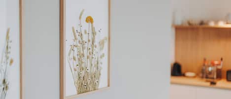 Una impresión botánica enmarcada en una pared, una cocina con armarios de madera y encimera, y un fondo desenfocado que sugiere un ambiente residencial.