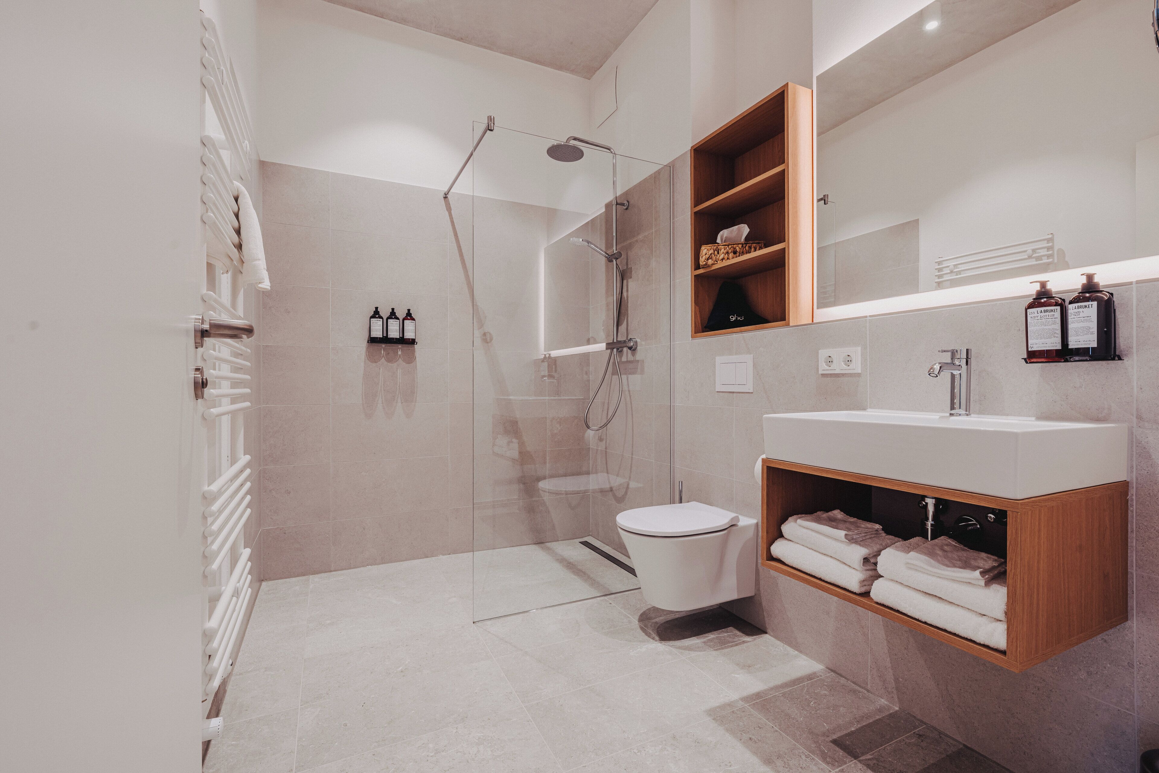 A modern bathroom with a glass-enclosed shower, a toilet, and a vanity with a mirror and shelves.