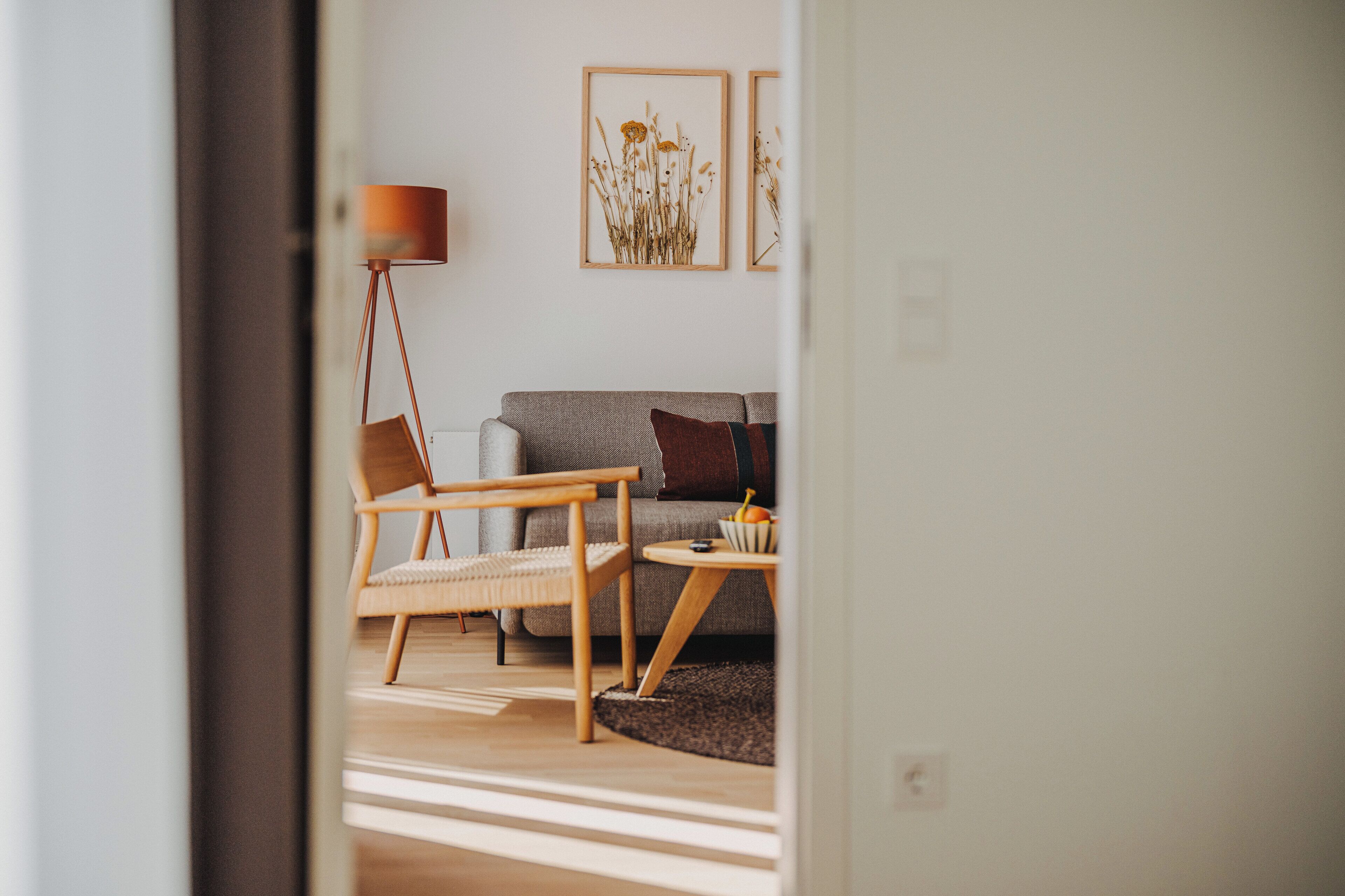 Ein modernes Wohnzimmer mit einer Couch, einem Holzstuhl, einer Stehlampe und gerahmten Kunstwerken an der Wand.