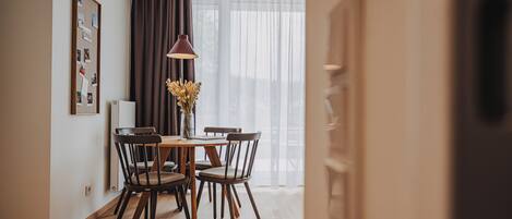A dining area with a wooden table and chairs, a pendant light, and a vase with flowers.