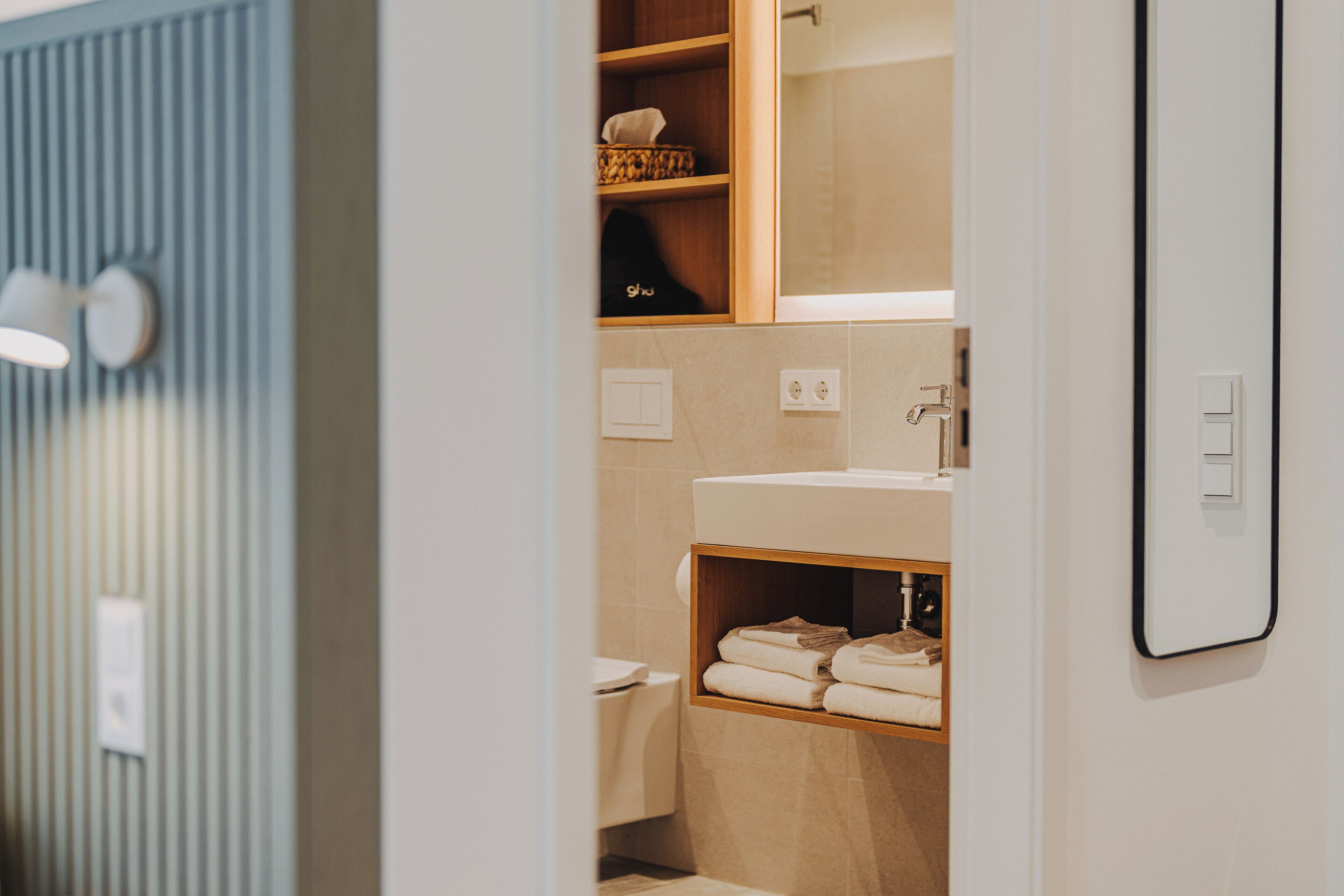 A modern bathroom with a wooden vanity, a mirror, and a towel rack.