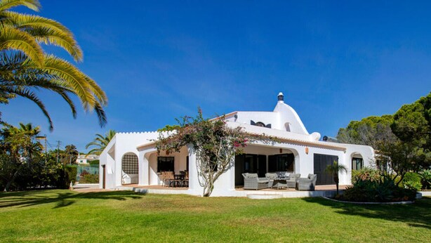 Eine weiße Villa mit überdachter Terrasse, umgeben von üppiger Vegetation und Palmen.