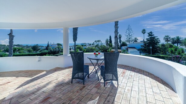 A covered outdoor seating area with wicker chairs and a table, overlooking a scenic landscape with trees and a view of the sea. - Villa Paraiso Beautiful villa in an enviable position (Carvoeiro)