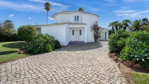 A white building with a circular design, a paved driveway, and surrounding greenery. - Villa Paraiso Beautiful villa in an enviable position (Carvoeiro)
