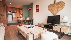 A modern living room with a wooden coffee table, a white sofa, a TV on a wooden stand, and a heart-shaped wall decoration.