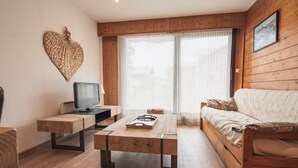A cozy living room with a wooden floor, a sofa, a coffee table, and a television on a wooden stand.