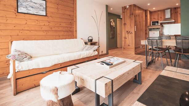 A modern living room with a wooden sofa, a coffee table, and a dining area with chairs and a kitchen counter.