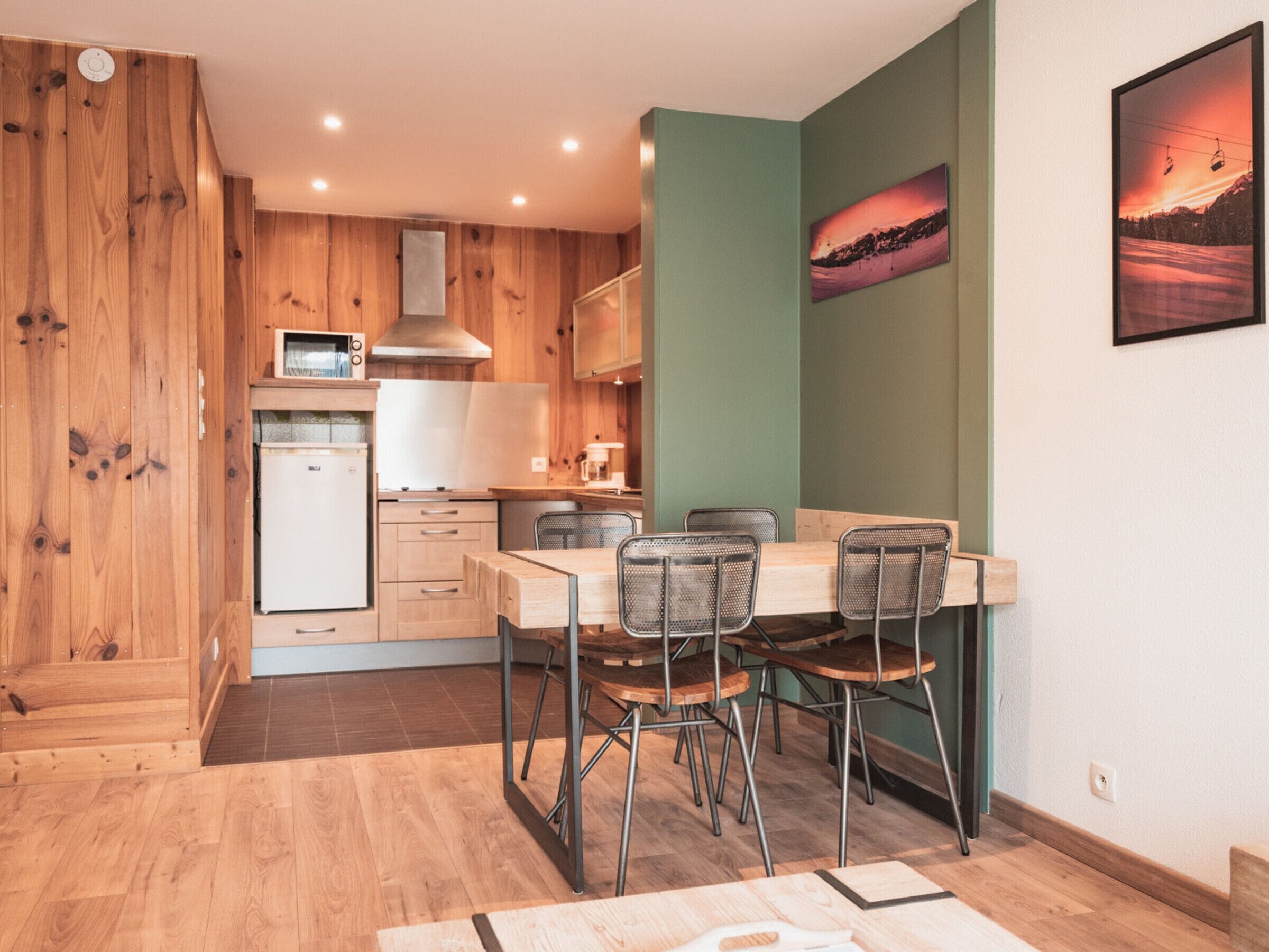 A compact kitchen with wooden cabinets, a refrigerator, and a dining area with a table and chairs.