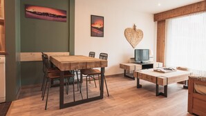 A modern living room with a wooden dining table, chairs, a TV, and artwork on the walls.
