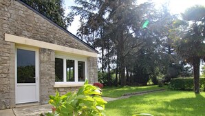 A stone building with a window and a door, surrounded by a well-maintained lawn and various plants. - Charming house in Normandy, pets allowed, parking (Hautteville-Bocage)