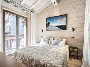 A bedroom with a large bed, wooden walls, a window with a view, and a painting on the wall.