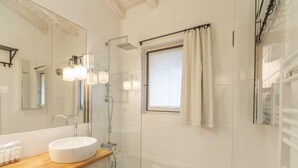 A modern bathroom with a white sink, a glass-enclosed shower, and a window with curtains.