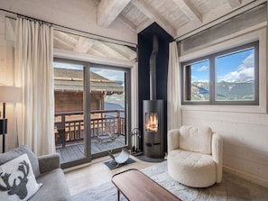Una habitación acogedora con chimenea, un sofá y vistas a una terraza de madera y montañas.