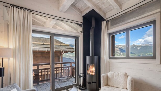 A cozy room with a fireplace, a sofa, and a view of a wooden deck and mountains.