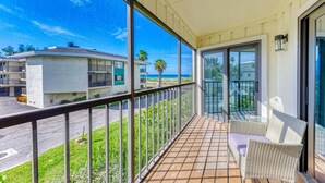 A balcony with a view of the ocean, a wicker chair, and a glass door. - Paradise Palms-private Beach Access-heated Pool-water Views From Every Room (Bradenton Beach)