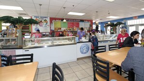 A food court with a counter displaying various food items, a menu board, and seating areas with tables and chairs. - Paradise Palms-private Beach Access-heated Pool-water Views From Every Room (Bradenton Beach)