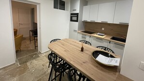 A compact kitchen with white cabinets, a wooden countertop, and a dining area with a table and chairs. - Vieux-nice 3 Pièces Confortable et Calme (Nice)