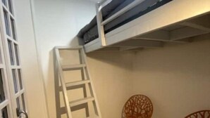 A room with a bunk bed, a ladder, two chairs, and a window with a metal grille. - Vieux-nice 3 Pièces Confortable et Calme (Nice)