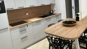 A modern kitchen with white cabinets, a wooden countertop, and a black sink. There is a dining table with chairs and a bowl on it. - Vieux-nice 3 Pièces Confortable et Calme (Nice)