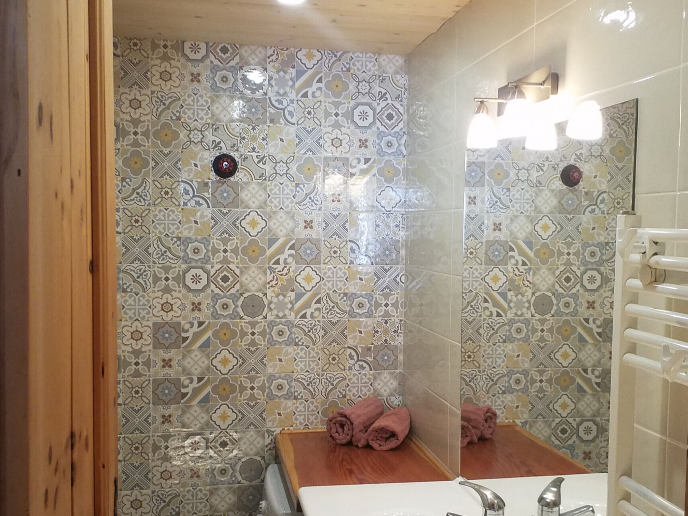 A bathroom with patterned tiles, a wooden bench, a sink, and a mirror.