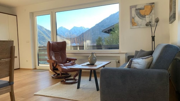 A modern living room with a large window, a leather chair, a grey sofa, and a small table with a decorative vase.
