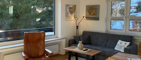 En moderne stue med læderlænestol, sofa, sofabord og spisebord. Store vinduer giver udsigt til omgivelserne.