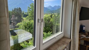 A room with a large window offering a view of mountains and greenery.
