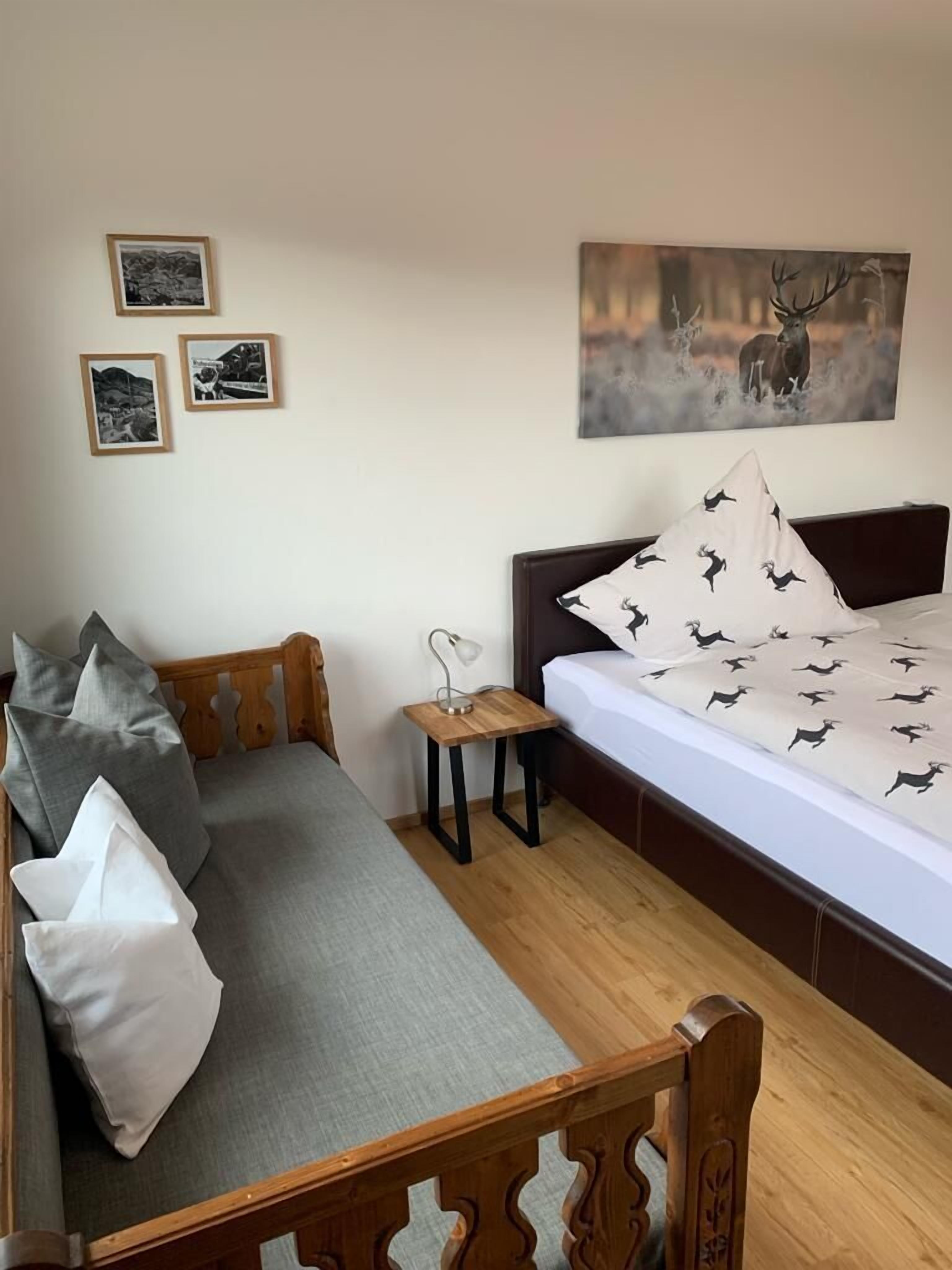 A bedroom with a bed, a wooden bench, a small table with a lamp, and three framed pictures on the wall.