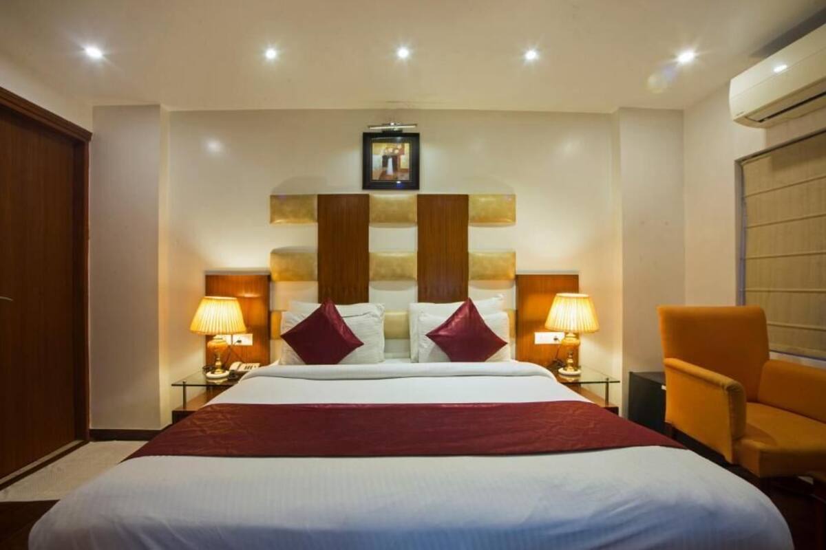 A hotel room with a large bed, two bedside lamps, a wooden headboard, a red throw blanket, and a wooden chair.