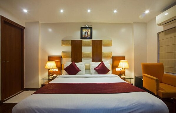A hotel room with a large bed, two bedside lamps, a wooden headboard, a red throw blanket, and a wooden chair.