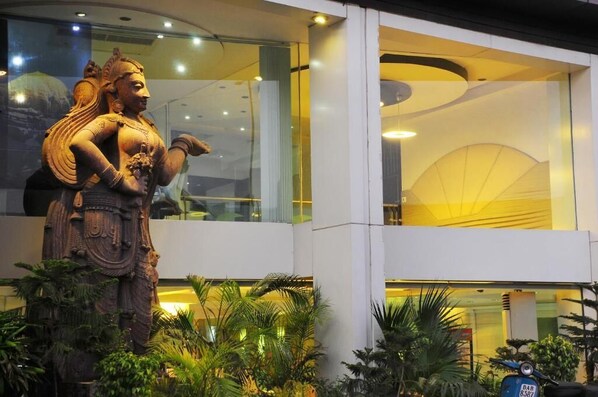 A statue of a deity in front of a modern building with glass windows and indoor plants.
