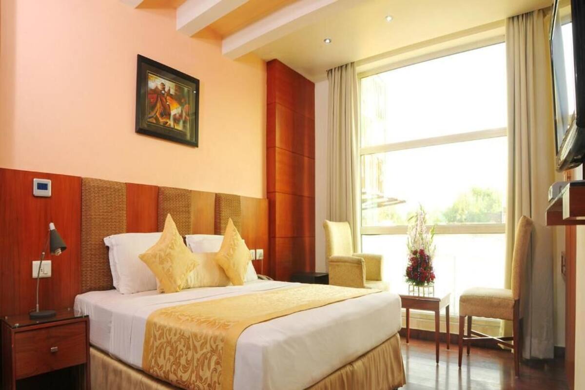 A hotel room with a large bed, a nightstand, a chair, a TV, and a window with curtains.