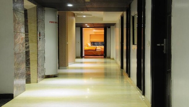 Un couloir d’hôtel avec un sol ciré, un panneau d’indication concernant la sécurité incendie, et un lit visible au loin.