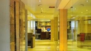 Un couloir d’hôtel avec un comptoir d’accueil, un espace salon et des murs en verre.