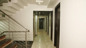 Un couloir d’hôtel moderne, avec un escalier sur la gauche, un sol ciré et une porte au fond.