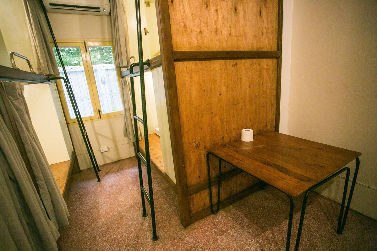 A room with a wooden table, a metal ladder, and a window with curtains.