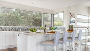 A modern kitchen with a large island, white cabinetry, and a view of trees through large windows.