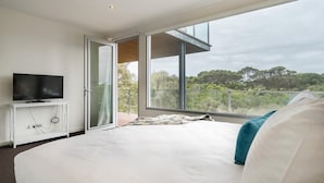 A modern bedroom with a large bed, a TV on a white console, and a balcony with a glass door.