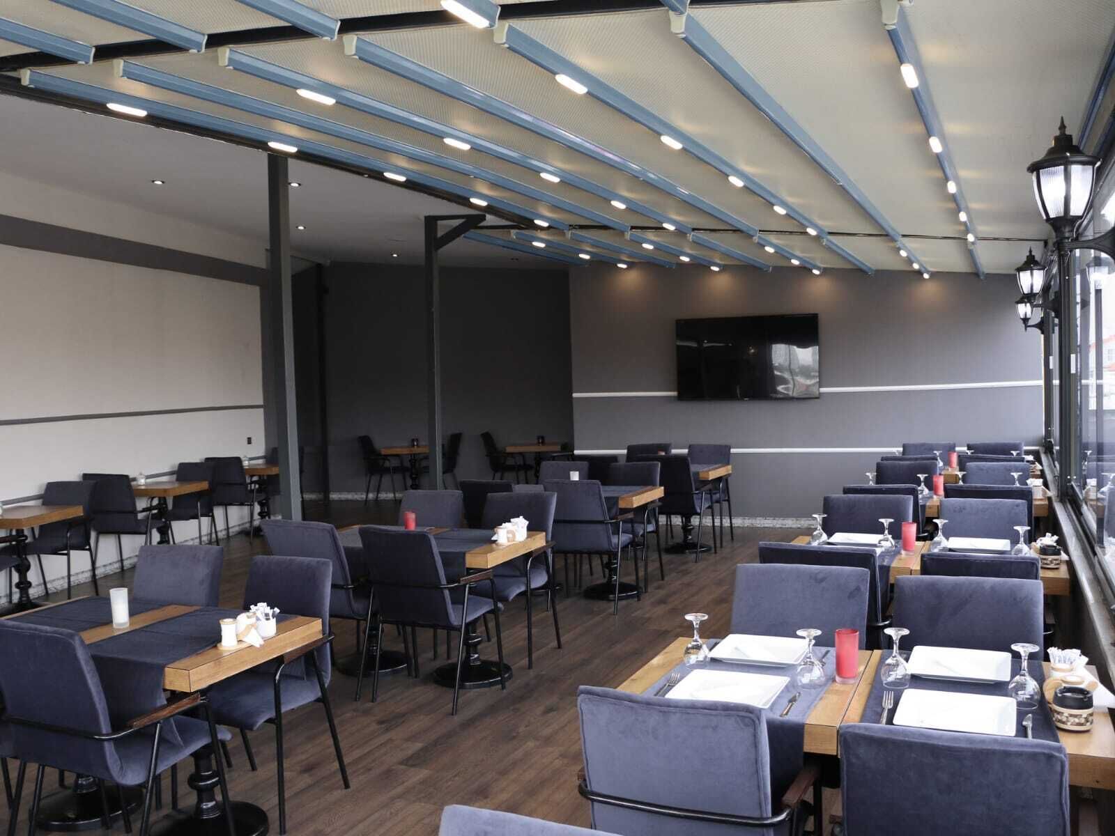 Un espace repas moderne, avec des tables et des chaises, un éclairage au plafond et un téléviseur à écran plat fixé au mur.