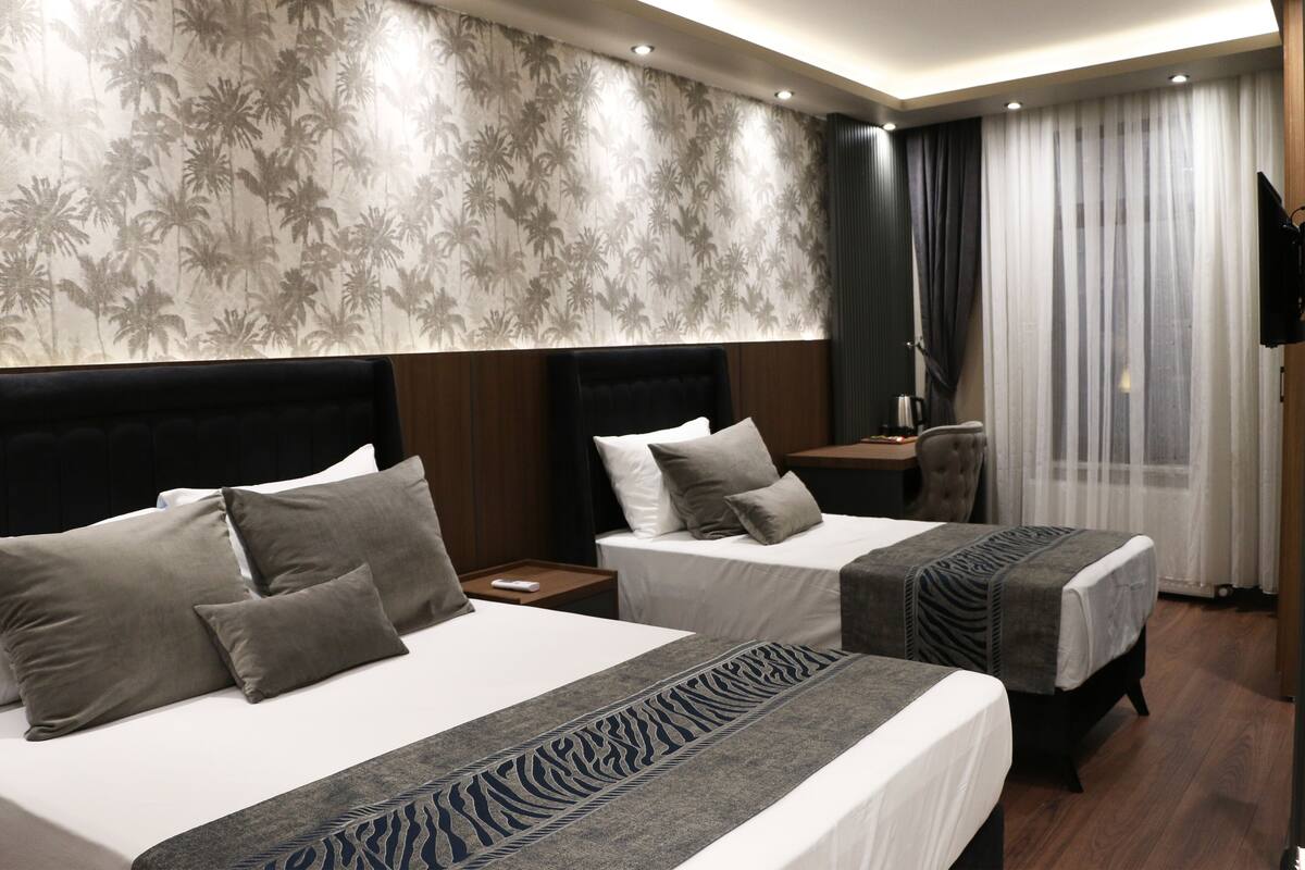 A hotel room with two beds, a large mirror, a flat-screen TV, and a window with curtains.