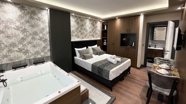 Una habitación de hotel moderna con una cama grande, un baño independiente con bañera, un escritorio con silla y un televisor montado en la pared.