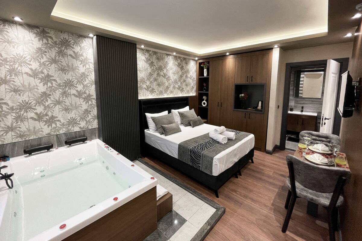 A modern hotel room with a large bed, a separate bathroom with a bathtub, a desk with a chair, and a TV mounted on the wall.